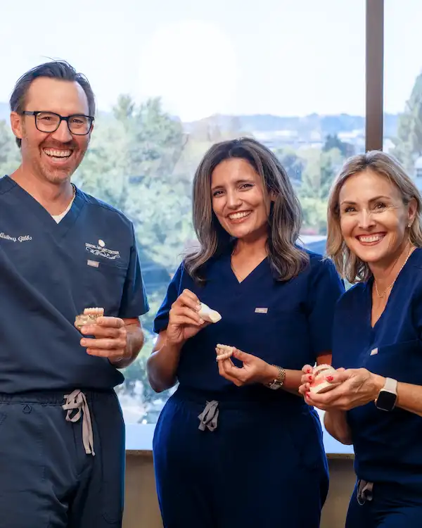 Dr. Gibbs and dental assistants at Dental Implant Center at Walnut Creek holding dental prosthesis and smiling  in Walnut Creek, CA.